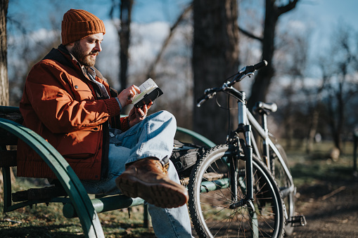 A peaceful scene of a man enjoying a book outdoors beside his parked bicycle, showcasing leisure in nature.