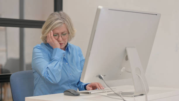 istock Old Businesswoman with Headache Working on Desktop Computer 2148513905