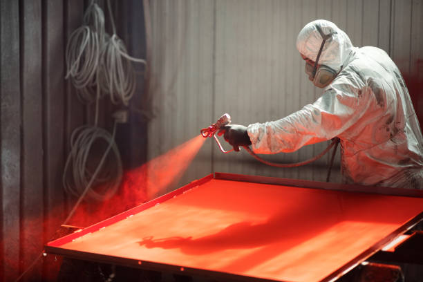 Closeup of an early 30's male using a compressor for spray painting steel plates at a factory facility.