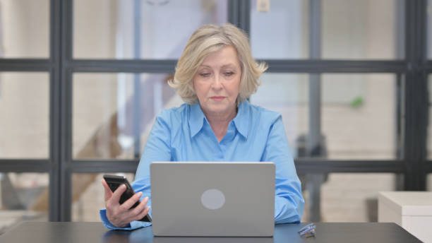 istock Old Businesswoman Using Phone and Laptop 2148515474