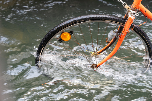 A bicycle is in the water with its tire missing. The water is murky and the bike is in the middle of it