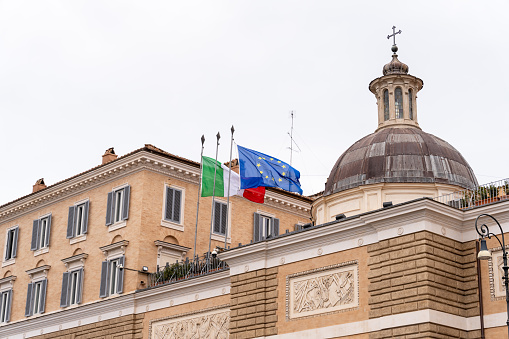 A building with a dome on top and flags flying on the roof