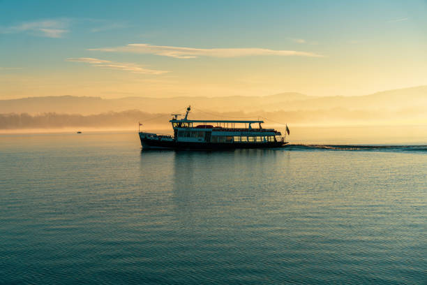 A boat is sailing on a calm lake at sunset. The sky is filled with clouds, and the water is still. The boat is the only thing visible in the scene, and it is moving slowly