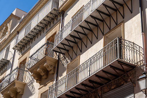 A building with a balcony has a lot of ironwork. The balconies are open and the building is tall