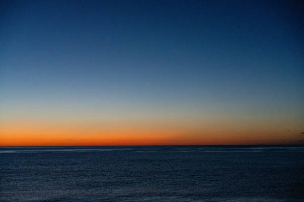 A blurry image of a blue ocean with a horizon line. The sky is a deep blue color with a few orange streaks