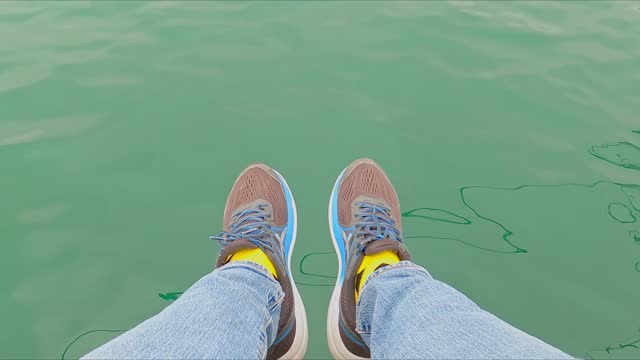 View of legs in jeans and sneakers dangling above the surface of the sea