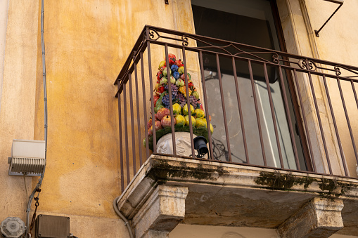 A balcony with a colorful flower arrangement on it. The flowers are in a vase and are placed on a railing. The balcony is on a building with a yellow wall