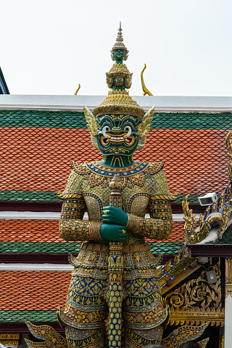 A statue of a green figure holding a sword. The statue is located in front of a building with a red roof