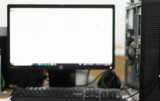 A computer monitor with a white screen in an office, a computer tower beside it, a white background, a blurred background, depth of field blur, shot from a low angle, professional photography