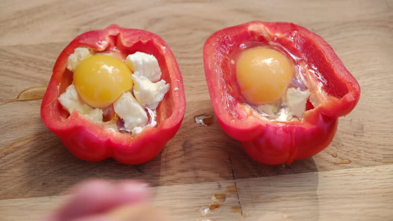Close up of male hands breaking or cracking one yellow egg into stuffed bell pepper with cheese on wooden board. Cooking outdoor food at spring day. Camp, adventure and vacation nature concept