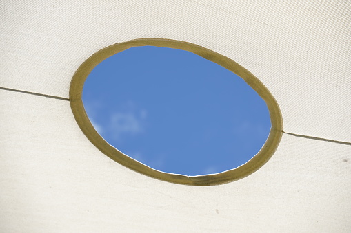 Abstract white interior fragment. Blue cloudy sky behind the round window