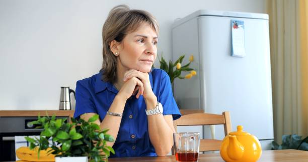 istock Pensive woman procrastinates at kitchen table, distant gaze. Conceptual procrastination, tea untouched, decision delayed. Procrastination theme, cinematic home setting, trendy lifestyle portrayal. 2148518858