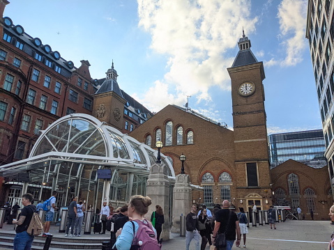 London, UK - 09.26.2021: Facade of the entrance of the Liverpool Street Station with passengers walking past and entering the station via an ironwork and glass structure under a blue sky