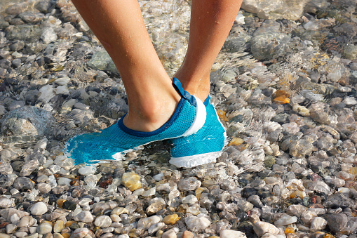 Feet of an 8-year-old boy standing in shallow sea wearing turquoise water shoes. Summer vacations activities. Water sports equipment for children