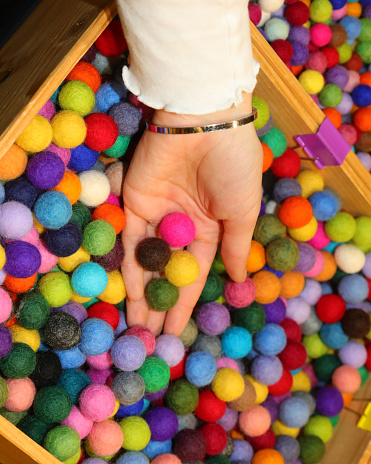 hand of a young girl holding colorful balls made of boiled wool to create a personalized necklace in the hobby shop