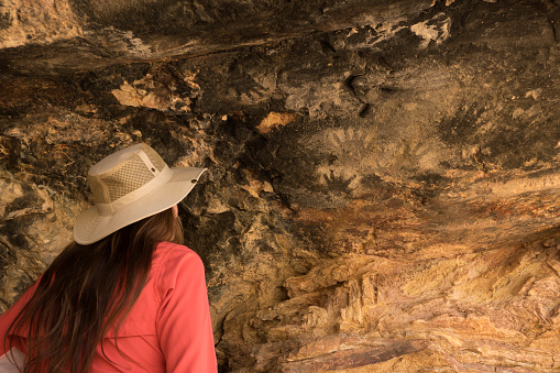 A woman with long hair and hat explores the prehistoric Mannos Arriba, a Native American rock shelter with hand prints and rock art in Big Bend Ranch State Park in west Texas.