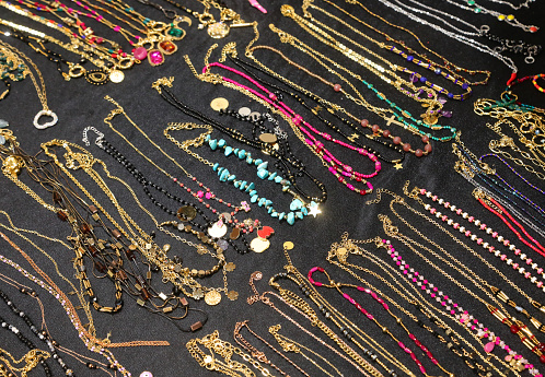 many necklaces and bracelets and anklets for women of golden metallic material with precious stones or pearls and pendants for sale in the shop in the shopping center