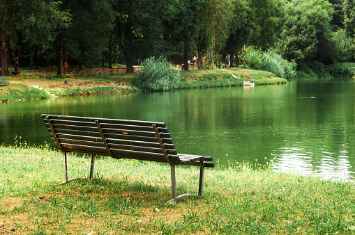 Outdoor wood chair in garden with pond, empty bench in quiet park