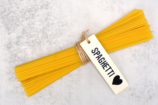 Raw spaghetti with wooden tag and string isolated on white background.