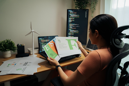 Engrossed in ESG strategy, a professional examines materials at her tech-adept workspace, a confluence of coding and corporate responsibility.