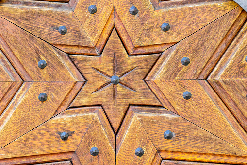 Close-up of old wooden gate with carved decoration in form of six-pointed star along with twelve rusty rivets on street of winemaking town Rust, Burgenland, Austria