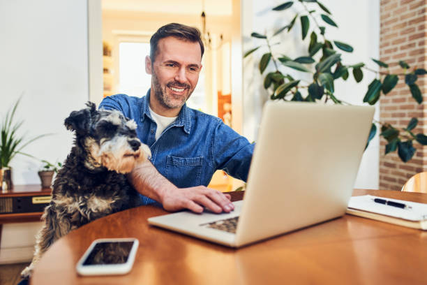 istock Happy man at home using laptop sitting together with his dog 2148535150