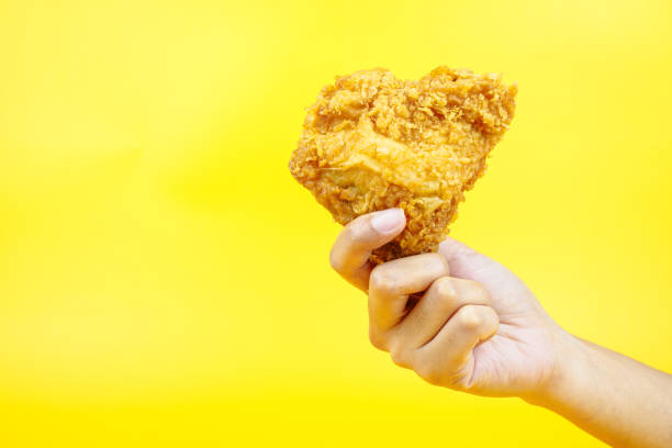 istock Female hand holding fried chicken on yellow background. 2148535420