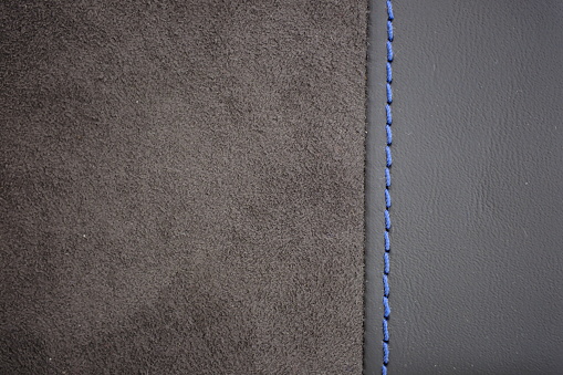 Blue contrast thread on a gray leather with black synthetic textile (Alcantara black) car seat close-up