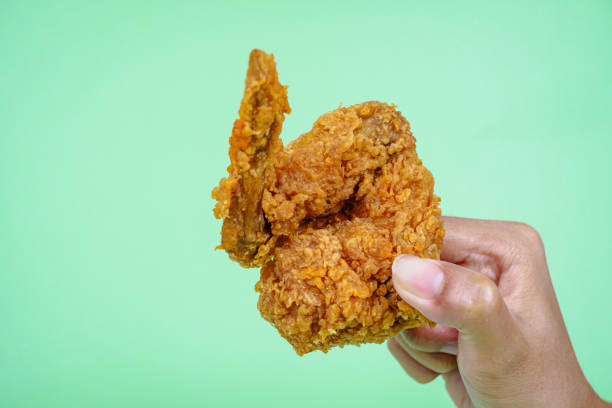 istock Female hand holding fried chicken on green background. 2148535427