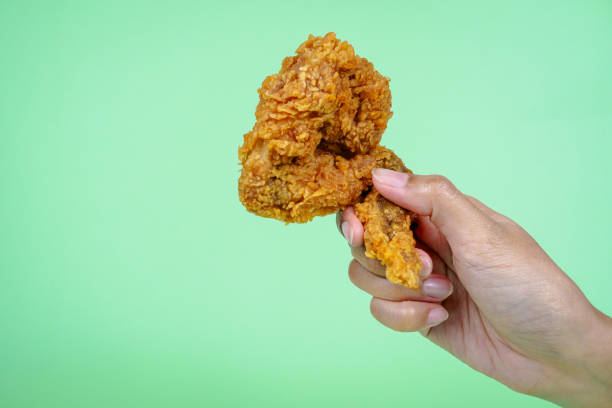 istock Female hand holding fried chicken on green background. 2148535437