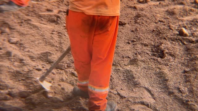 Workers in orange uniforms preparing the street soil to receive paving