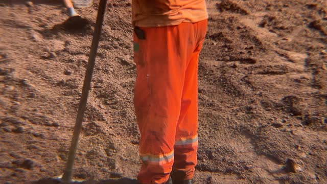 Workers in orange uniforms preparing the street soil to receive paving