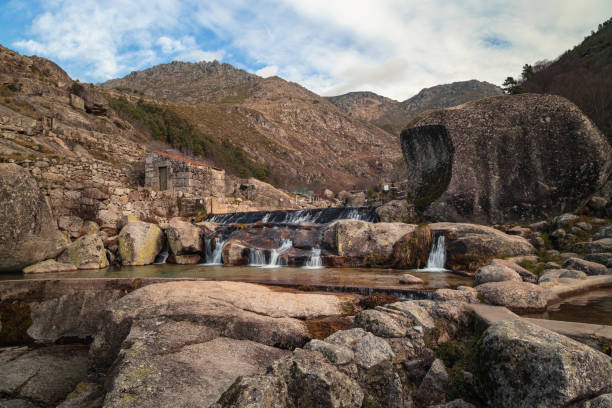 Serene mountain river landscape with misty peaks and stone ruins, located in Serra da Estrela Natural Park, Portugal