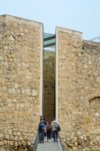 Tarragona, Spain - April 13, 2024: A narrow path flanked by ancient stone walls in Tarragona, where people enjoy a walk, combining historical architecture and daily life.