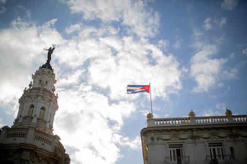 The Cuban flag flying from the roof of a colonial style building on Paseo de Prado, with a spire of the \