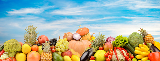 Panoramic photo fruits and vegetables on background white clouds and blue sky.