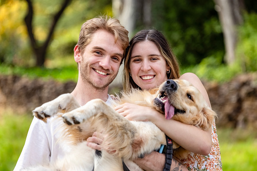 Portrait of happy young couple in the park with their pet Golden Retriever, front view, background with copy space, full frame horizontal composition