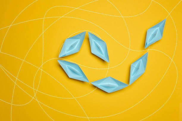 Blue paper boats move one after another on a yellow background, top view