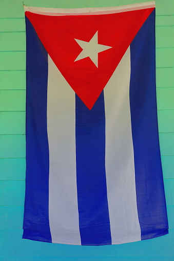 Cuban flag hanging on the light green painted wall of a porch in a bohio -Cuban hut- of a vernacular tobacco farm, land of the UNESCO World Heritage listed Valle de Viñales Valley. Pinar del Rio-Cuba.