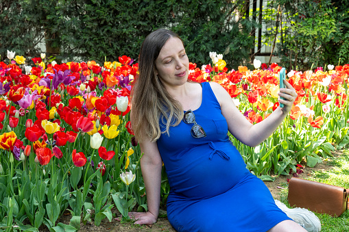 Beautiful pregnant  woman feeling lovely doing selfie and smile in the park
