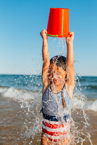 Cheerful little girl having so much fun pouring other with the bucket from the ocean on her summer vacation in Algarve Portugal