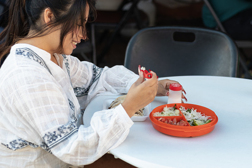 26-year-old tourist woman, smiling and enjoying meat tacos with vegetables at a local Mexican food restaurant; customers eating traditional street food