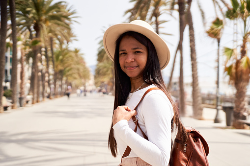 Cheerful portrait of an African American female traveler doing tourism in her beach holidays, looking at camera smiling. Copy space.