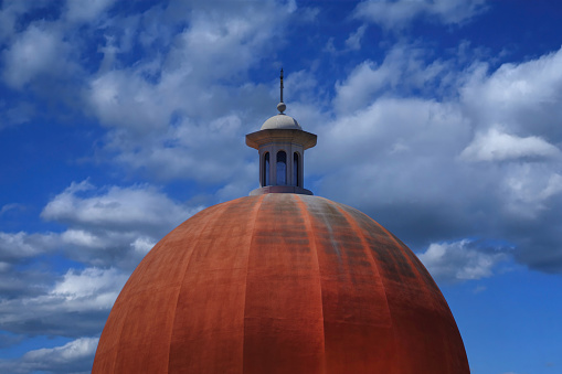 Reddish cupola roof under blue sky with clouds