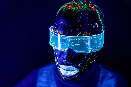Portrait of a man painted in fluorescent UV colours with cyberglases looking at camera