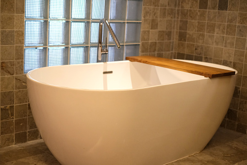 Close-up shot of clean modern white bathtub with a wooden tray placed on top of it