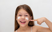 Portrait of smiling child pointing at cream on cheeks as sun protection concept