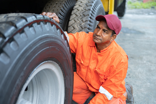 Asian Indian Male Driver checking the condition of the truck tyre