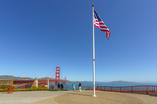 San Francisco, California, April 9, 2024. American flag flying high with the Golden Gate Bridge and visitors in the background.