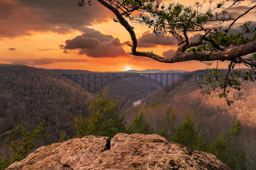 Witness the breathtaking beauty of the New River Gorge Bridge bathed in the fiery hues of a West Virginia sunset. This awe-inspiring image captures the iconic landmark's grandeur against a dramatic twilight sky. Perfect for showcasing the natural wonders of Appalachia and the state's stunning landscapes.